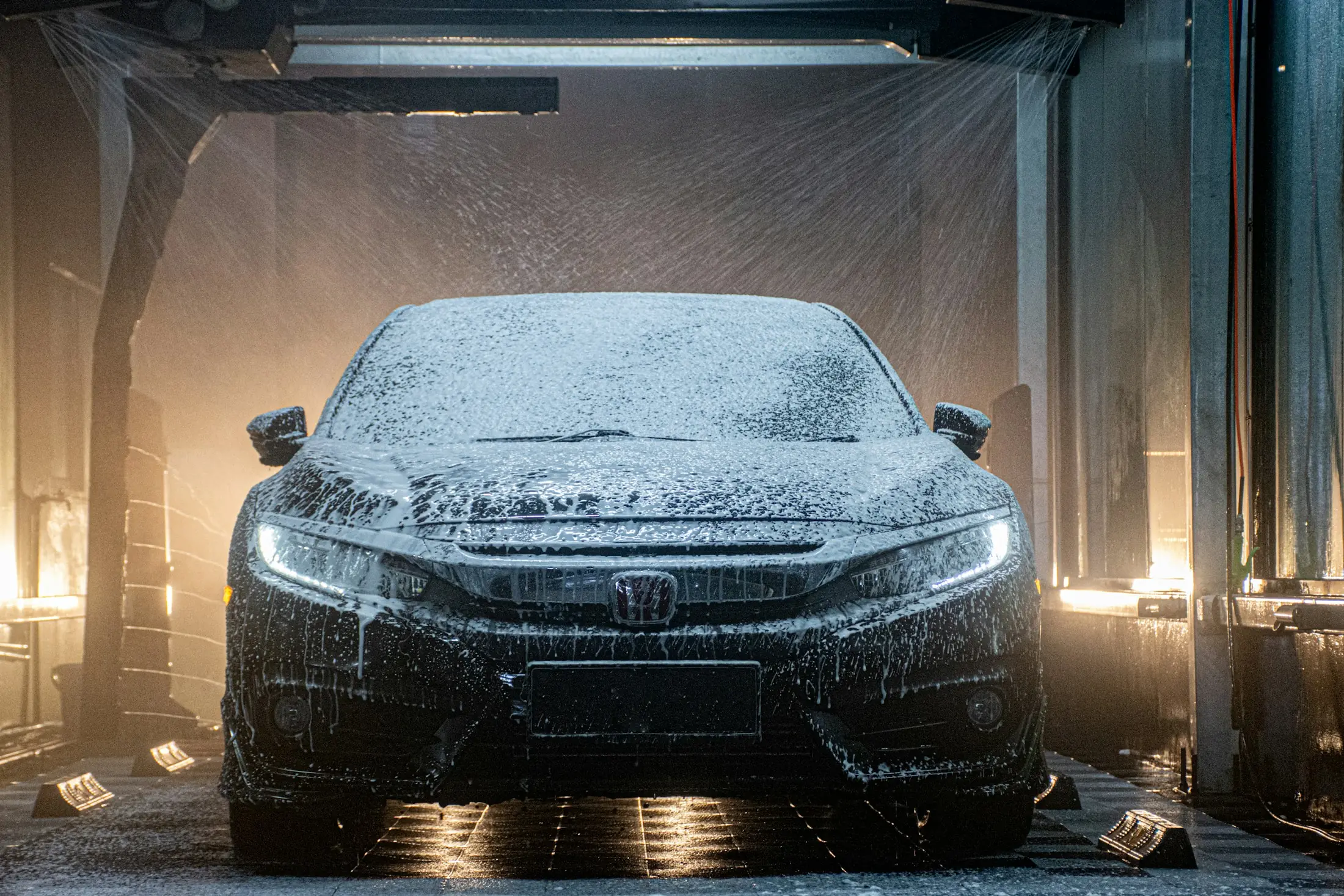 Sedan covered in snow foam inside a wash bay