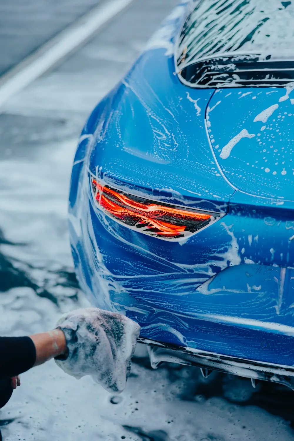 Hand washing a blue car covered in foam