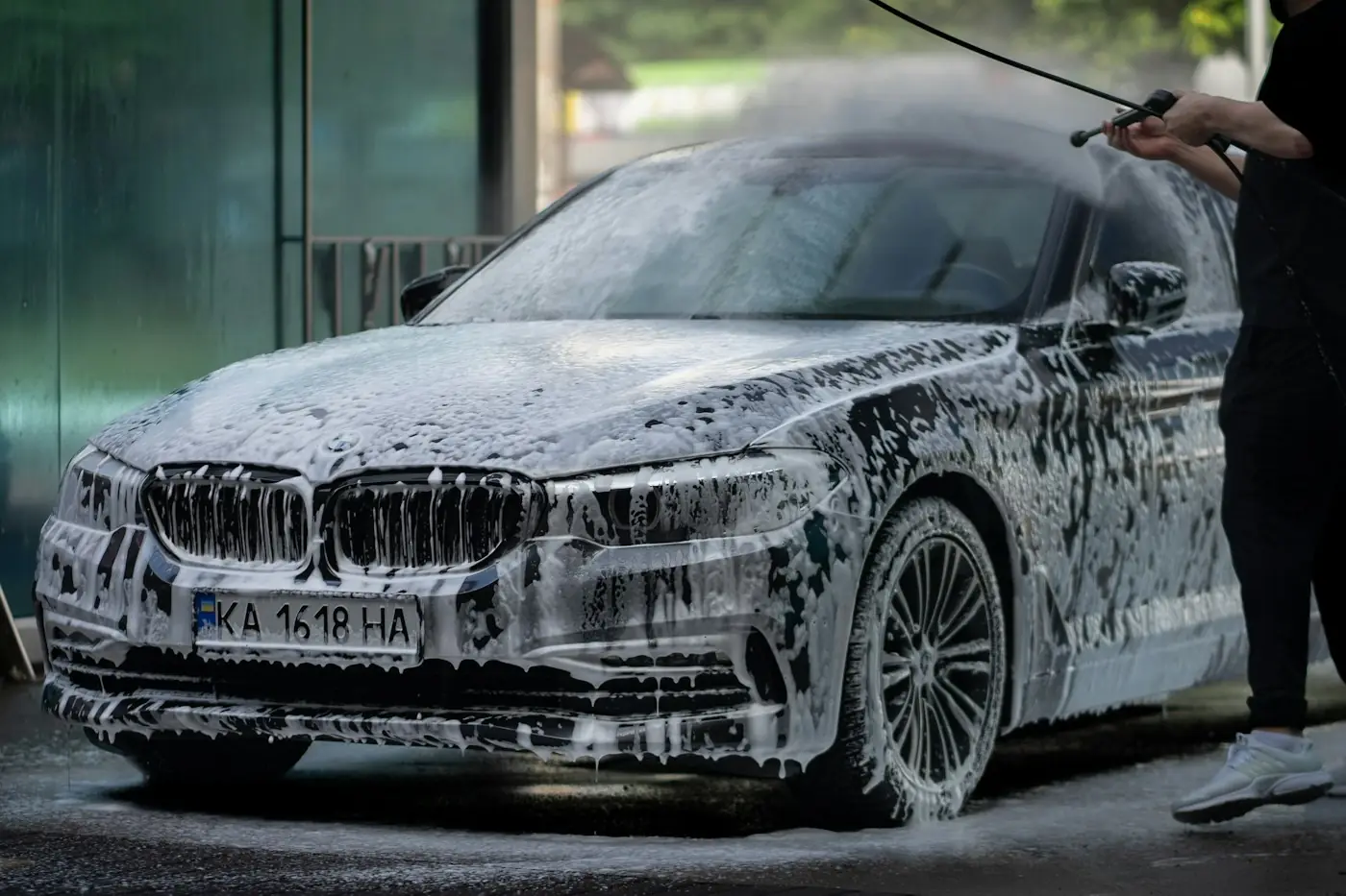 Sedan covered in foam being rinsed with a pressure washer